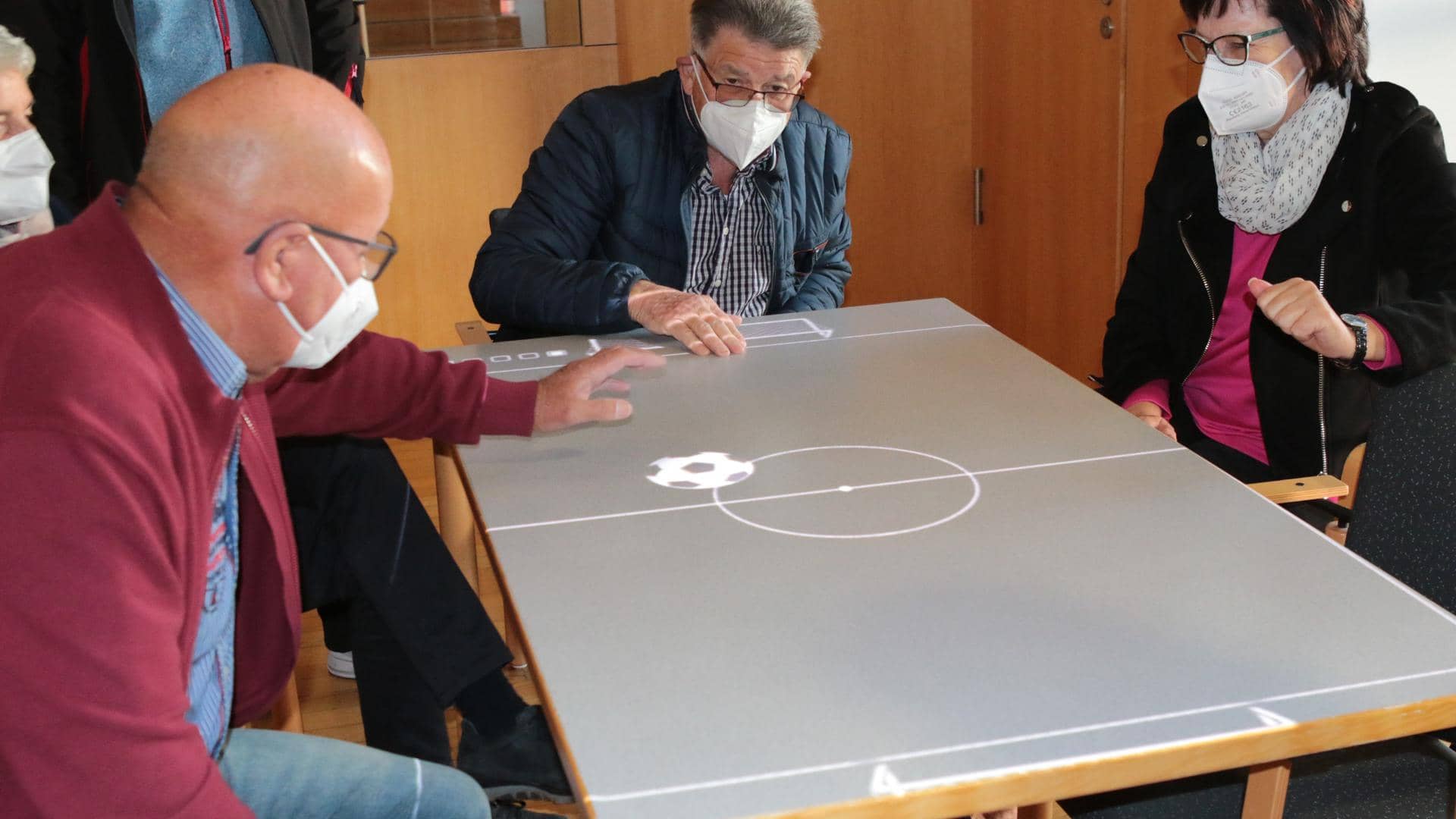 Two men and a woman at a table with a virtual soccer field