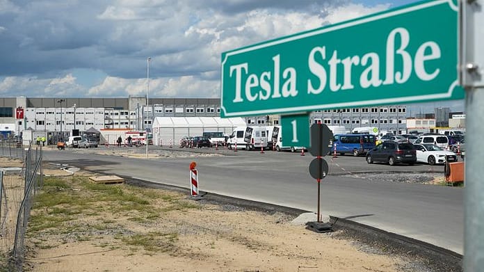 Das Straßenschild "Tesla Straße 1" steht an der Zufahrt zum Baugelände der Tesla Fabrik. (Quelle: dpa/Jörg Carstensen)