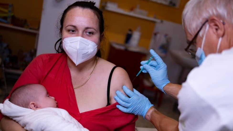 A doctor gives a vaccine against the coronavirus disease (COVID-19) to a woman who holds a baby in her arms, at his office in Berlin, Germany, on November 2, 2021.
