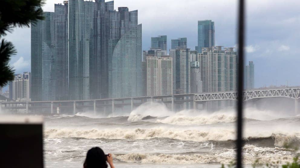 Woman taking a photo of waves with Busan skyline in the background