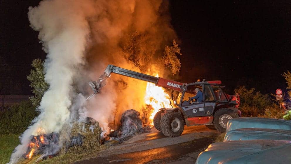 A farmer separates bales of burning hay with a loader