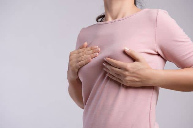 A woman's hand examining lumps on her chest for signs of breast cancer on a gray background.  health care