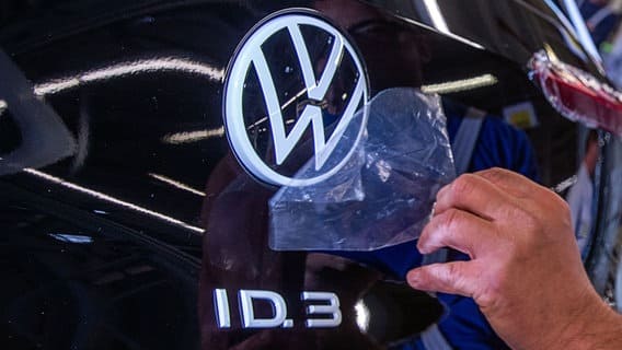 A staff member removes a protective film from the VW logo on the assembly line of the ID.3 electric vehicle production.  © dpa - Bildfunk Photo: Jens Büttner