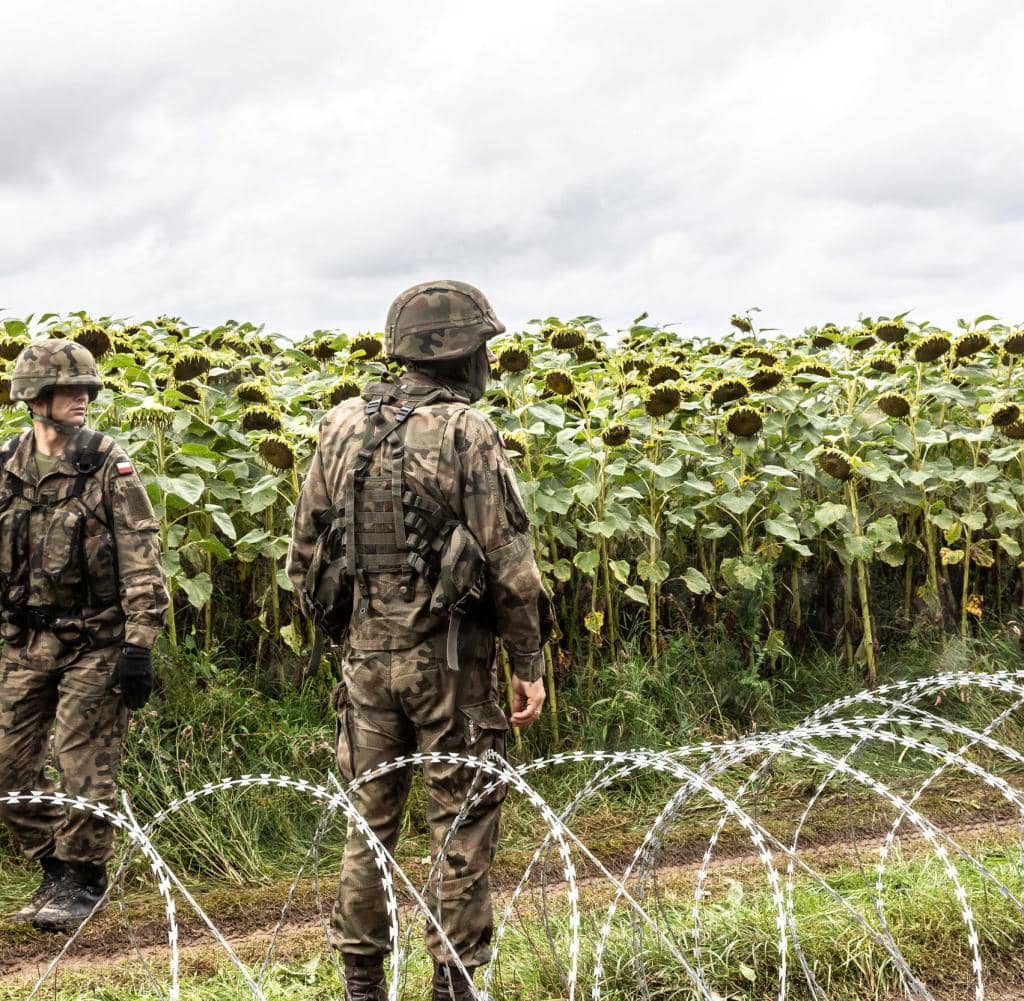 Polish soldiers stand in front of a fence on the border with Belarus.  Refugee movement fueled by dictator Lukashenko creates tension between neighboring countries